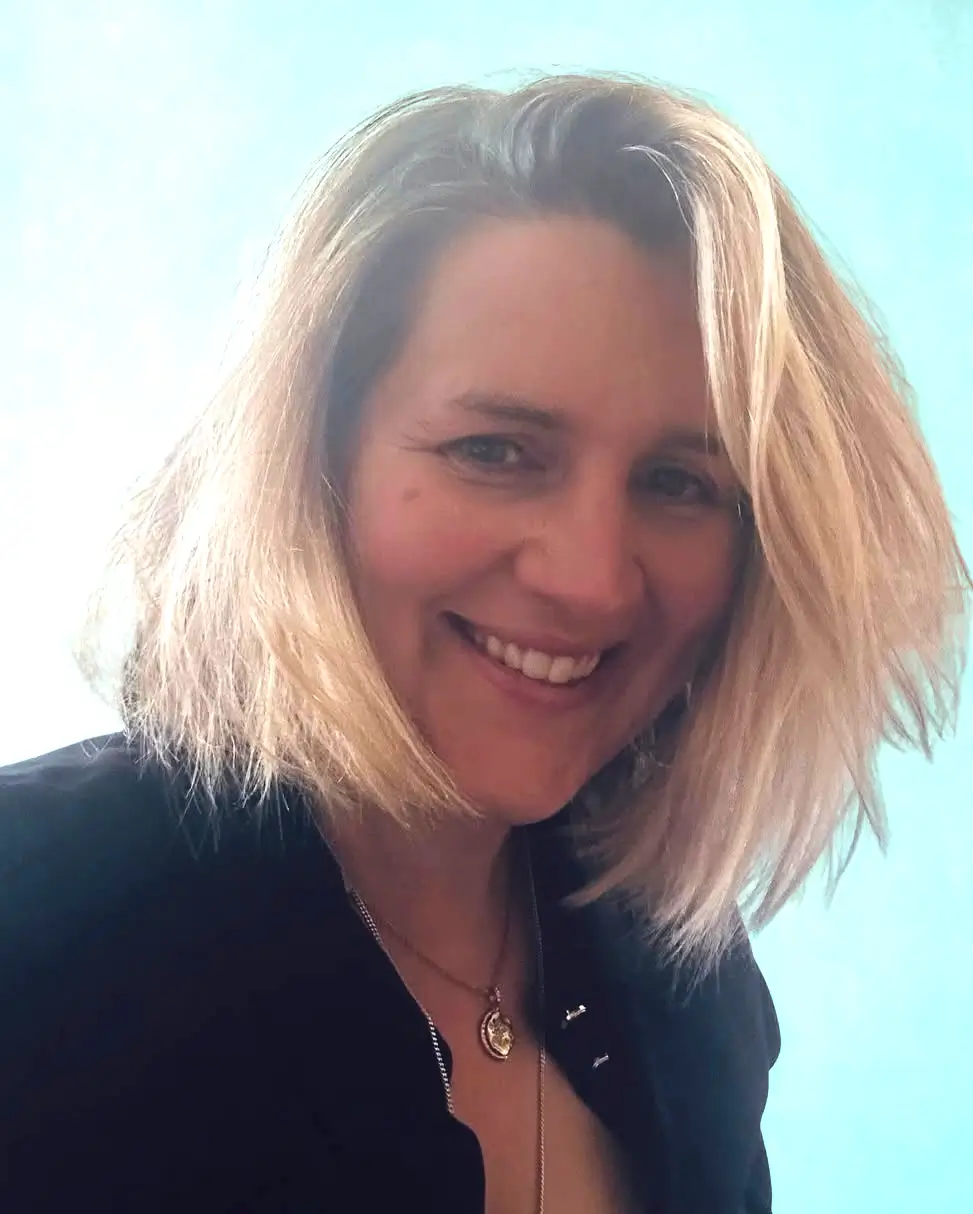 Woman smiling with blonde hair and necklace.